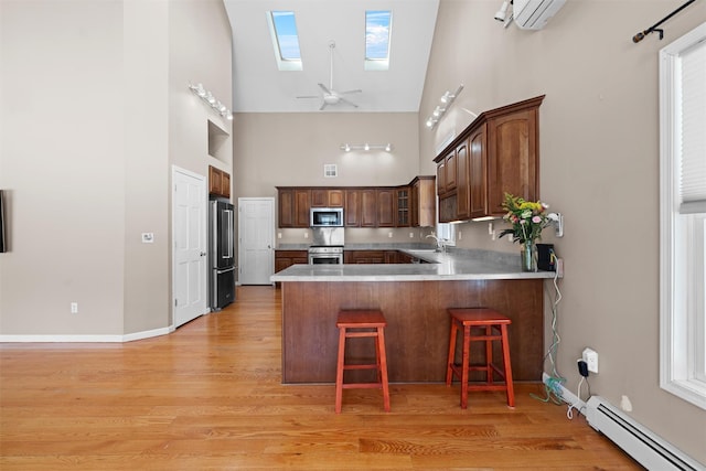 kitchen featuring a breakfast bar area, a baseboard radiator, appliances with stainless steel finishes, glass insert cabinets, and a peninsula