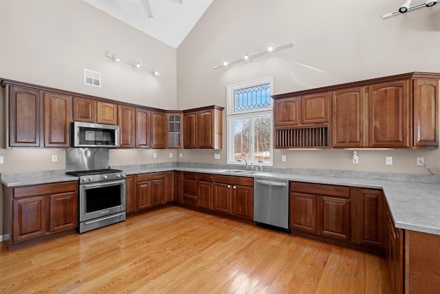 kitchen featuring stainless steel appliances, light countertops, glass insert cabinets, a sink, and high vaulted ceiling