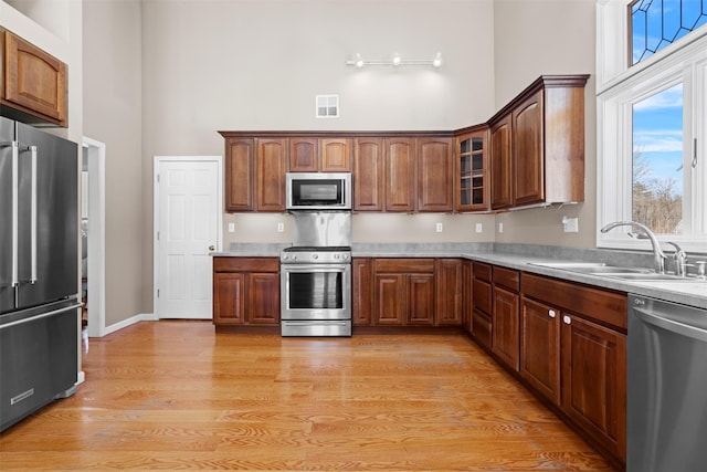 kitchen with stainless steel appliances, light countertops, visible vents, glass insert cabinets, and a sink