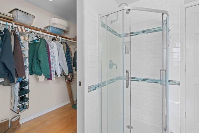 bathroom featuring a stall shower, a spacious closet, baseboards, and wood finished floors