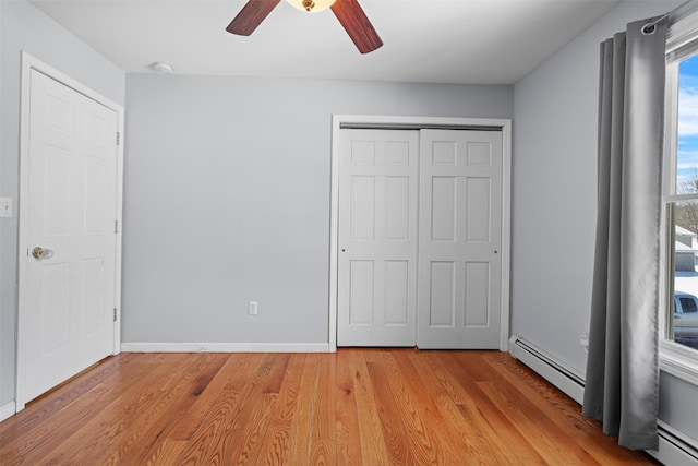 unfurnished bedroom with light wood-style flooring, baseboards, baseboard heating, and a closet