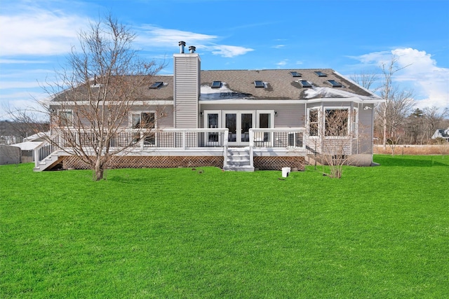 rear view of property with a deck, french doors, roof with shingles, a lawn, and a chimney