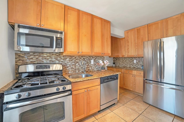 kitchen featuring a sink, light stone counters, appliances with stainless steel finishes, light tile patterned floors, and decorative backsplash