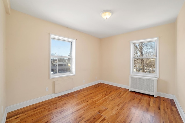 spare room with radiator, baseboards, and light wood-type flooring