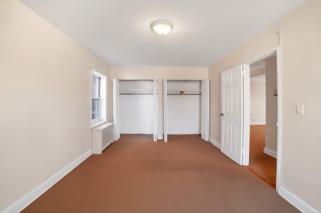 unfurnished bedroom featuring radiator, two closets, and baseboards