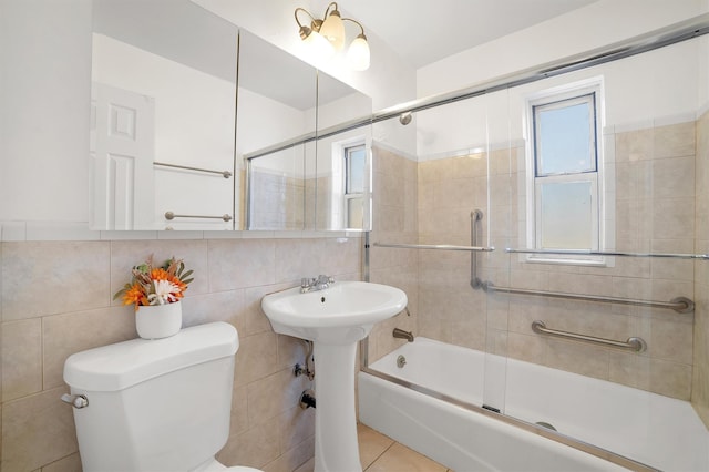 full bath featuring toilet, tile patterned floors, tile walls, enclosed tub / shower combo, and a sink