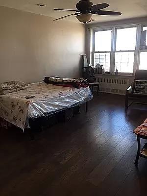 bedroom featuring dark wood-type flooring, radiator heating unit, and ceiling fan