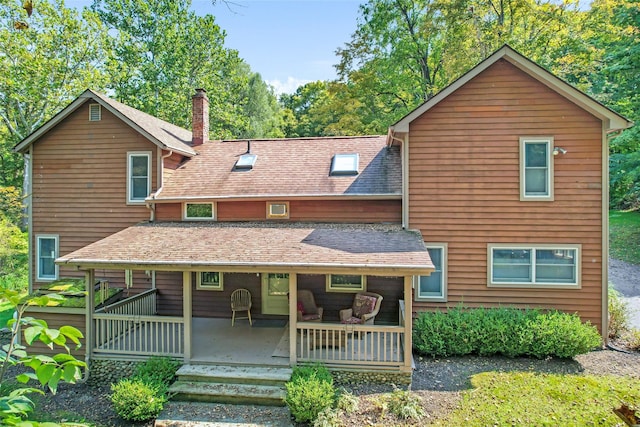 view of front of home with a porch, roof with shingles, and a chimney