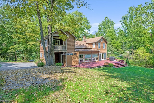 rear view of house featuring a lawn, a chimney, a wooden deck, and a balcony