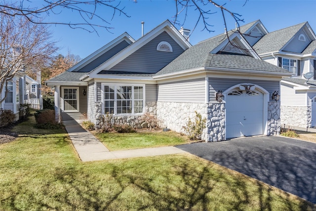 view of front of house with an attached garage, stone siding, driveway, roof with shingles, and a front yard