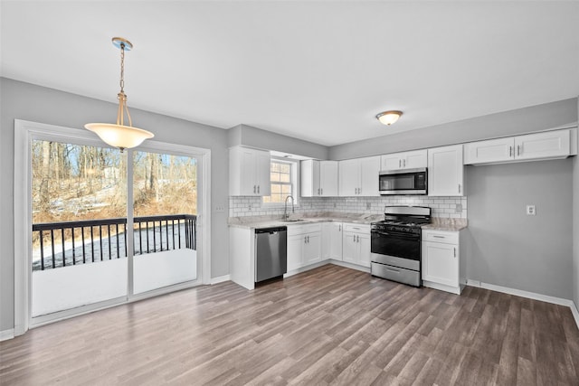 kitchen with sink, stainless steel appliances, tasteful backsplash, white cabinets, and decorative light fixtures