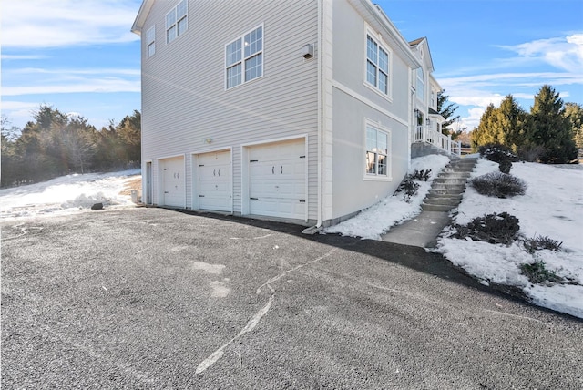 view of snow covered exterior featuring stairs, aphalt driveway, and an attached garage