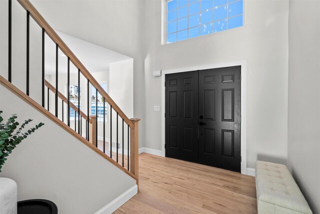 foyer with baseboards, light wood-style flooring, a high ceiling, and stairs