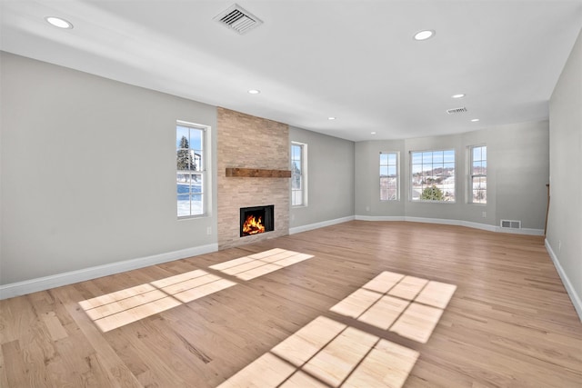 unfurnished living room with light wood-style flooring, visible vents, baseboards, and a stone fireplace