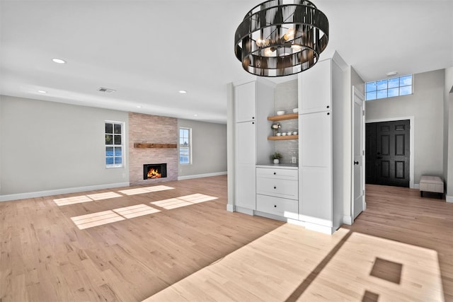 unfurnished living room featuring light wood finished floors, a fireplace, recessed lighting, and an inviting chandelier