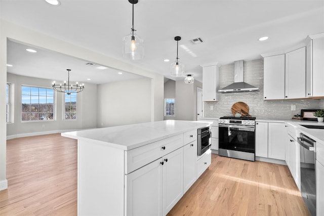 kitchen with wall chimney exhaust hood, a center island, hanging light fixtures, stainless steel range with gas cooktop, and white cabinetry