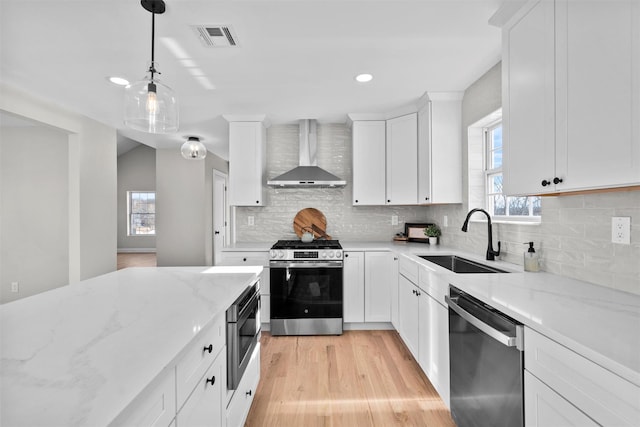 kitchen featuring stainless steel appliances, a sink, white cabinets, light stone countertops, and wall chimney exhaust hood