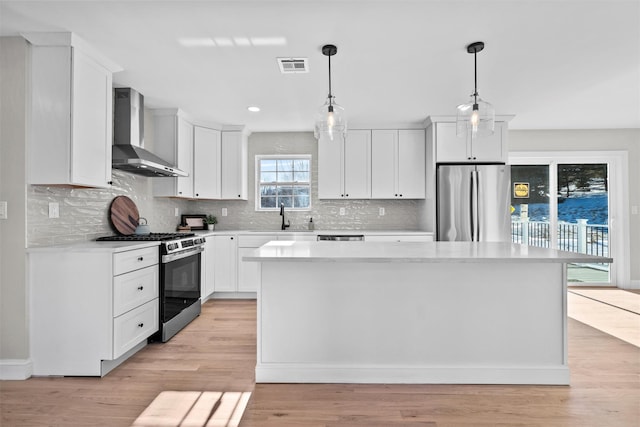 kitchen with light countertops, appliances with stainless steel finishes, white cabinetry, a kitchen island, and wall chimney exhaust hood