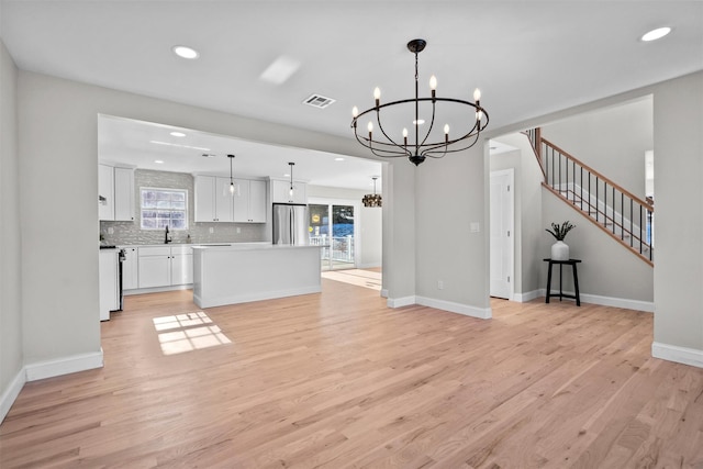 unfurnished living room with stairs, light wood-type flooring, visible vents, and an inviting chandelier