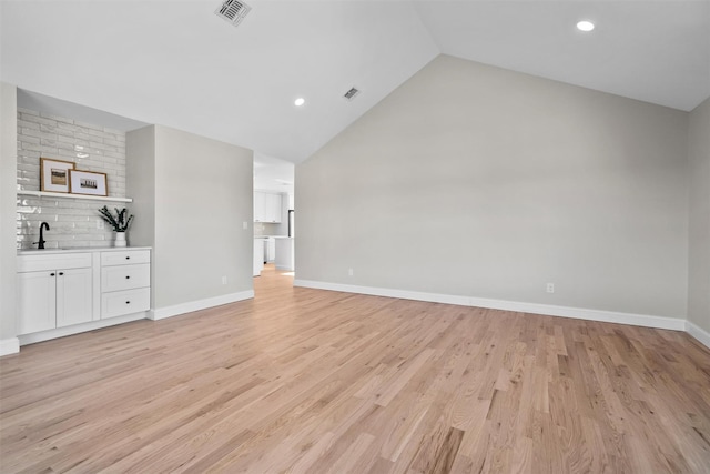 unfurnished living room featuring light wood-type flooring, visible vents, a sink, and baseboards