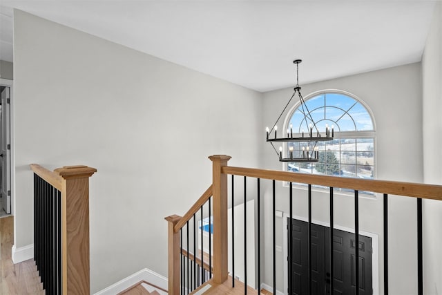 corridor with baseboards, light wood-type flooring, an upstairs landing, and a notable chandelier