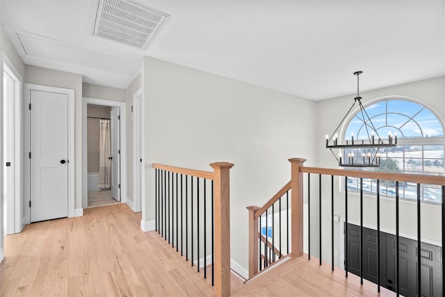 corridor with visible vents, light wood-style floors, an upstairs landing, a chandelier, and baseboards