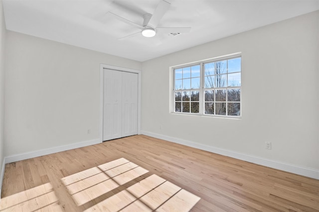 unfurnished bedroom featuring light wood-style flooring, baseboards, ceiling fan, and a closet