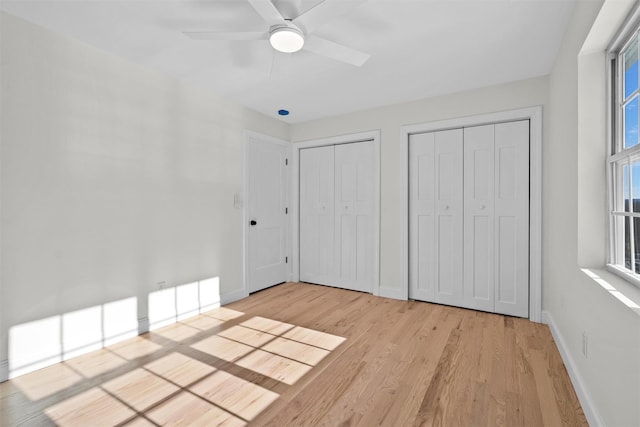 unfurnished bedroom featuring baseboards, ceiling fan, light wood-style floors, and multiple closets