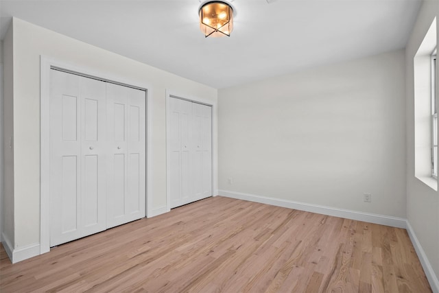 unfurnished bedroom featuring light wood-type flooring, baseboards, and two closets