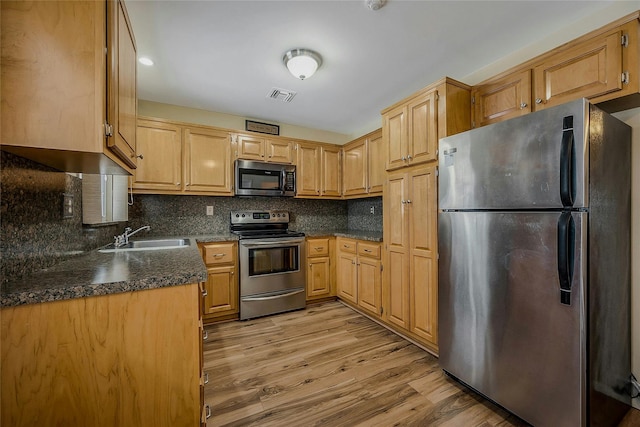 kitchen with dark countertops, visible vents, appliances with stainless steel finishes, a sink, and light wood-type flooring