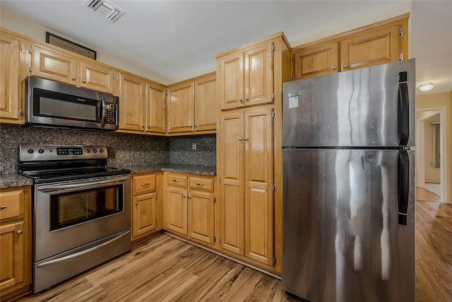 kitchen with dark countertops, visible vents, backsplash, light wood-style flooring, and appliances with stainless steel finishes