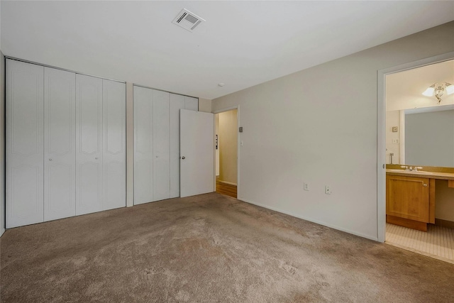 unfurnished bedroom featuring ensuite bathroom, light colored carpet, visible vents, and multiple closets