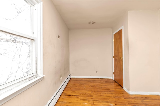 hall with a baseboard heating unit, baseboards, and light wood finished floors