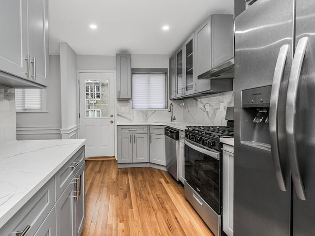 kitchen with stainless steel appliances, gray cabinetry, light stone counters, and light hardwood / wood-style floors