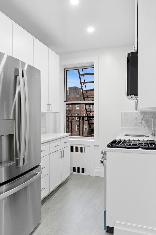 kitchen featuring radiator, tasteful backsplash, white cabinets, stainless steel fridge with ice dispenser, and white gas range oven