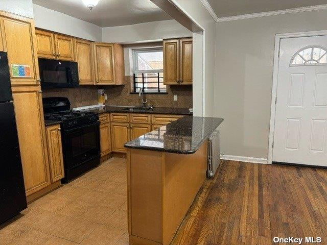 kitchen with sink, dark stone countertops, ornamental molding, kitchen peninsula, and black appliances