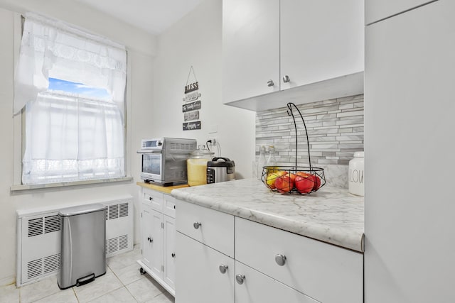 kitchen with light tile patterned flooring, heating unit, white cabinetry, tasteful backsplash, and refrigerator