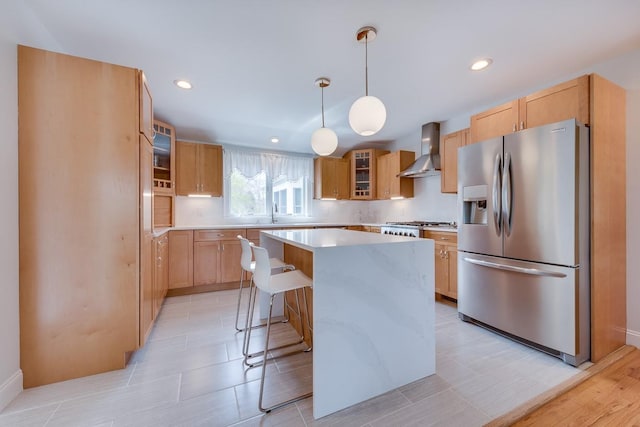 kitchen featuring a kitchen island, a breakfast bar, pendant lighting, stainless steel fridge, and wall chimney range hood