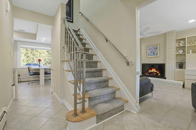 stairway featuring a fireplace, baseboard heating, ceiling fan, tile patterned flooring, and baseboards