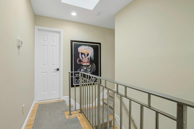 corridor with recessed lighting, a skylight, an upstairs landing, baseboards, and light wood-style floors