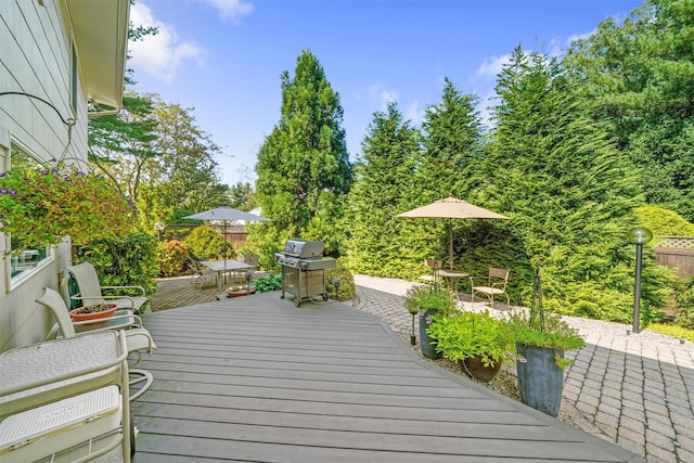 wooden deck featuring outdoor dining space, a patio area, a grill, and fence