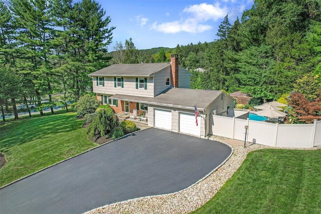 colonial home with a front lawn, fence, an attached garage, and aphalt driveway