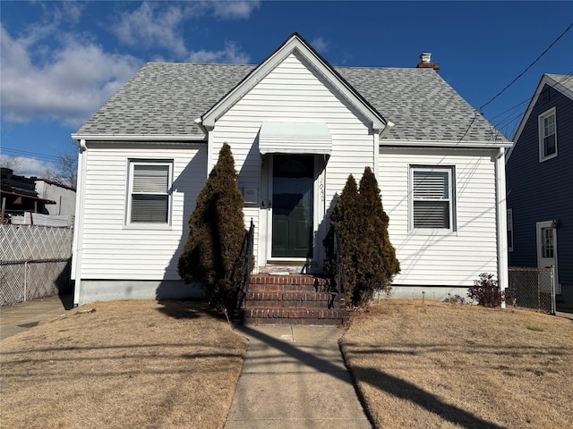 bungalow-style house with entry steps, a shingled roof, a front lawn, and fence