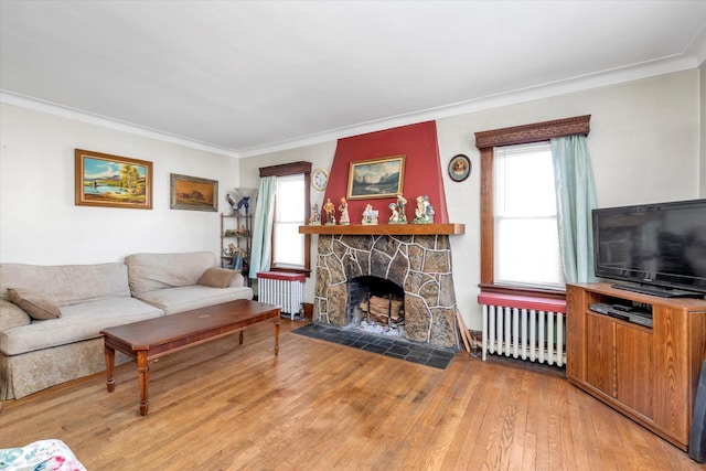 living room with ornamental molding, a stone fireplace, radiator, and hardwood / wood-style floors