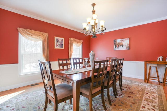 dining room with plenty of natural light, wood finished floors, an inviting chandelier, and crown molding