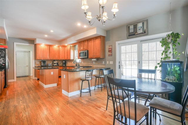 kitchen with light wood-style flooring, appliances with stainless steel finishes, brown cabinets, tasteful backsplash, and an inviting chandelier