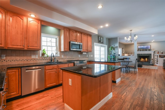 kitchen with a sink, a kitchen island, open floor plan, appliances with stainless steel finishes, and pendant lighting