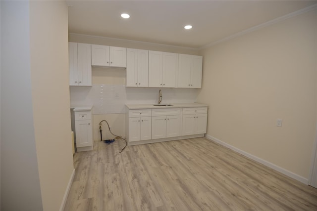 kitchen featuring light wood-type flooring, sink, white cabinets, crown molding, and decorative backsplash