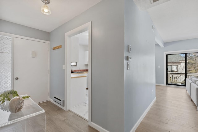 hallway with light wood finished floors, baseboards, and baseboard heating