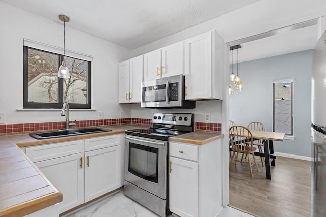 kitchen featuring tile countertops, white cabinetry, stainless steel appliances, and a sink